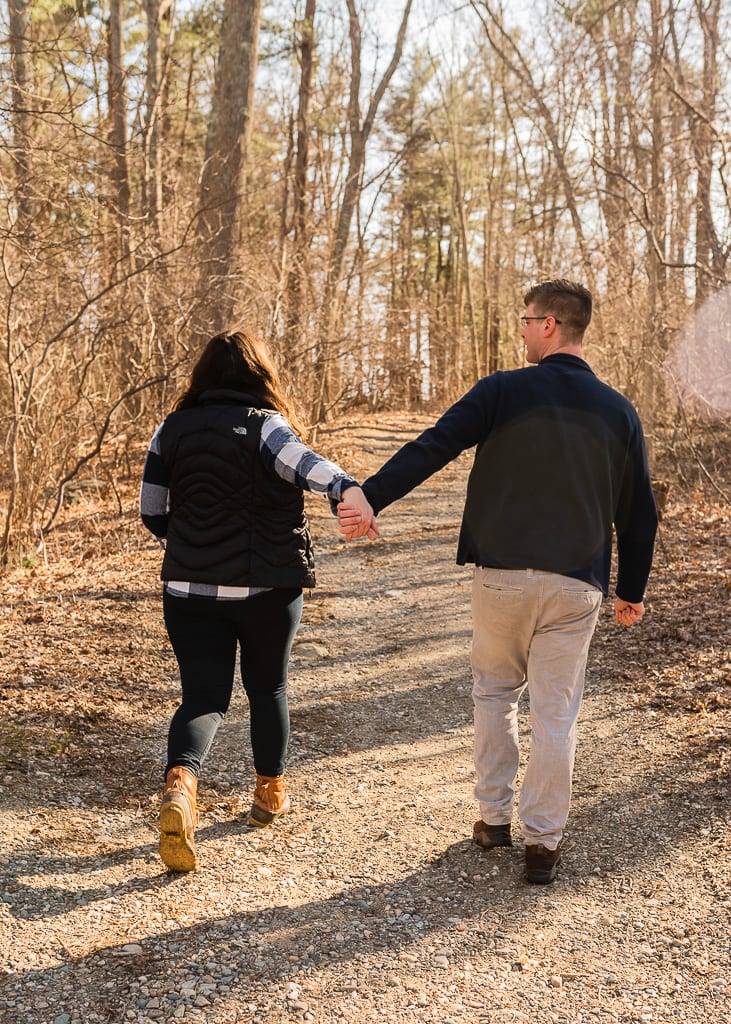 A couple walking hand in hand on a sunlight wooded trail