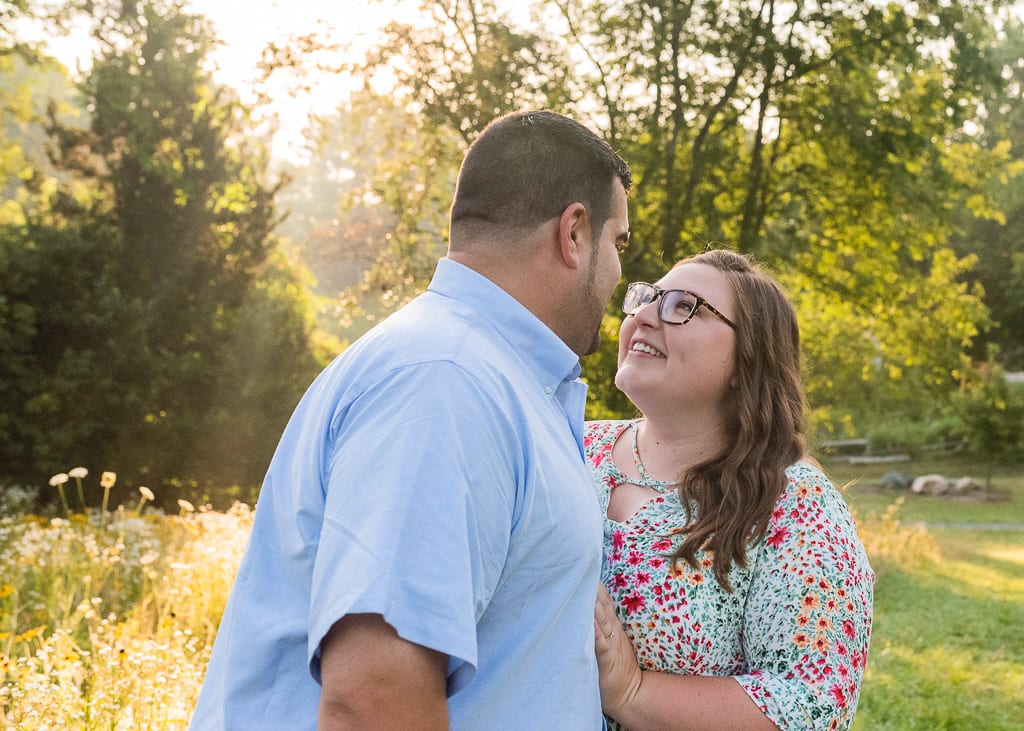Women looks lovingly at husband in field with sunlight